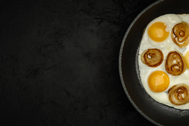 istock fresh fried eggs with onion rings in a frying pan on a black textured plaster background. top view. artistic dark moody photo with copy space for creative layout 1298981315
