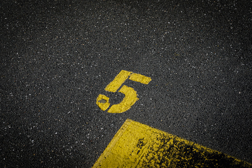 sign on the asphalt, yellow painted number five on grey street, yellow lines like a corner on the road, space for text