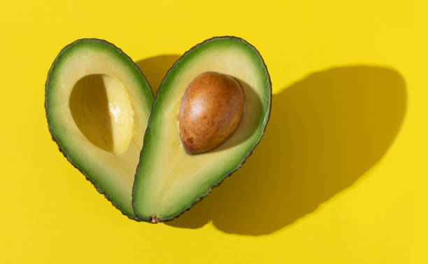 Avocado halves as heart shape with hard shadow on yellow background Avocado halves as heart shape close up with hard shadow on yellow background, healthy fats for heart health concept food styling stock pictures, royalty-free photos & images