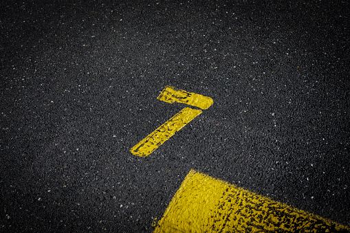 sign on the asphalt, yellow painted number seven on grey street, yellow lines like a corner on the road, space for text