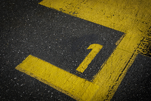 sign on the asphalt, yellow painted number one on grey street, yellow lines like a corner on the road, space for text