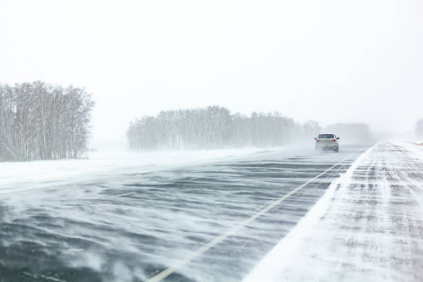 Car moves along an asphalt road during a snow storm.