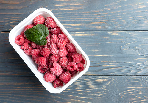 Frozen raspberries in a container on a wooden background with place for text.