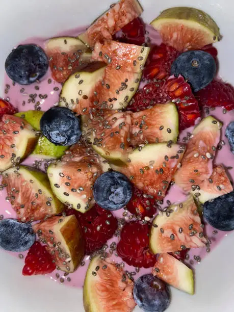 A bowl filled with yoghurt and colorful fruit is visible. The organic fruit is cut up and and is ready to eat. The fruit is fresh and delicious.