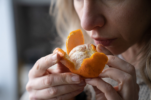 Mujer enferma tratando de detectar el olor de la mandarina fresca naranja, tiene síntomas de Covid-19, virus corona photo