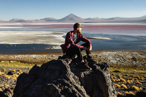 kaukasischer mann sitzt und schaut auf die malerische aussicht auf laguna colorada in altiplano, bolivien - laguna colorada stock-fotos und bilder