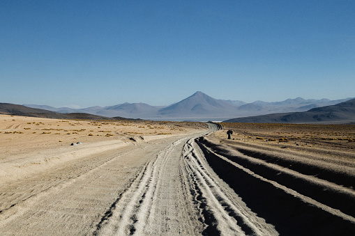 Road through the desert with mountain and volcano picks on the background at Altiplano in Bolivia