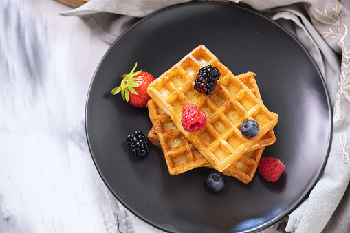 Homemade waffles served with fresh berry fruits and drizzled with maple syrup