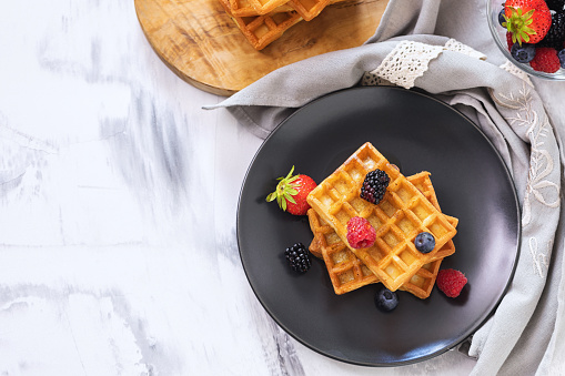 Homemade waffles served with fresh berry fruits and drizzled with maple syrup