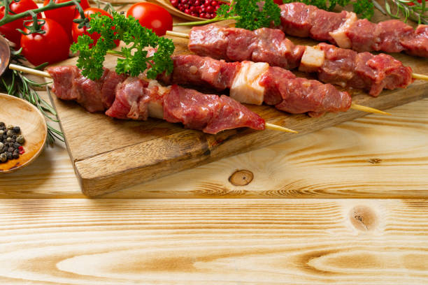 istock Raw kebab from meat on a wooden background with vegetables. 1298994148