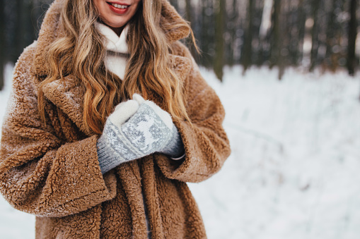 Young woman in fur coat, gloves and scarf in snowy forest. High quality photo