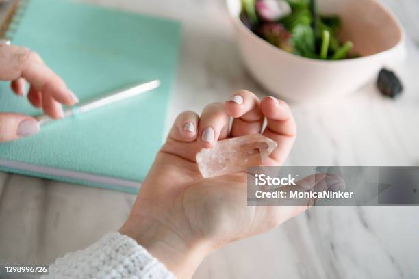 Hand Of Woman Holding Healing Crystals With Notebook In Background Stock Photo - Download Image Now