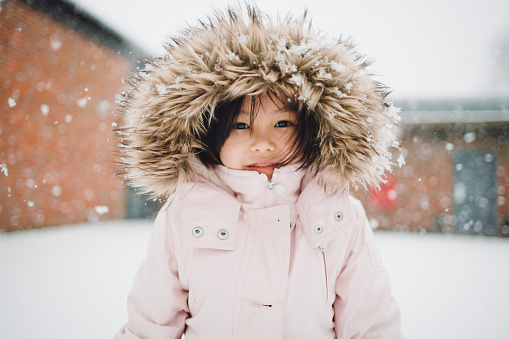 Winter portrait of a beautiful little girl looking at the camera and having a lot of fun in snow.