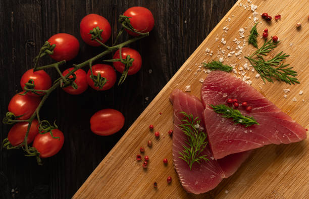 Freshly cut tuna fillets with tomato lying on a wooden cutting board