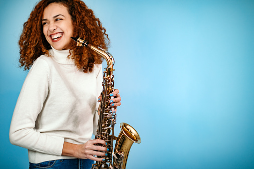 Woman standing in front of blue background and holding saxophone