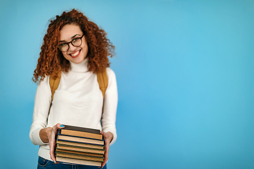 Woman standing in front of blue background holding books