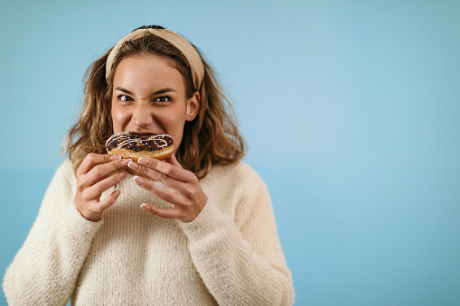 Woman standing in front of blue background and eating donut