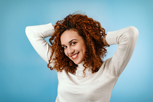 Woman standing in front of blue background playing with hair