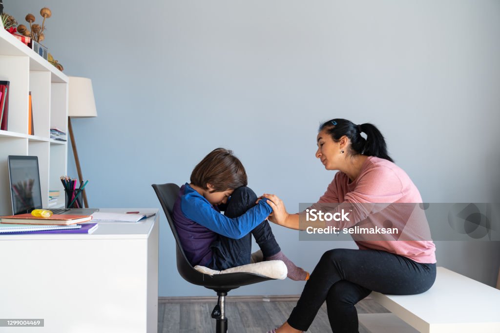 Mother Talking To Bored Schoolboy Having E-learning Photo of mother talking to her bored schoolboy son having online education during Coronavirus pandemic quarantine. Mother has black hair and is asian. Shot indoor with a full frame mirrorless camera. Mental Health Professional Stock Photo