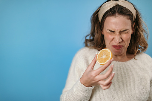 Woman standing in front of blue background eating lemon