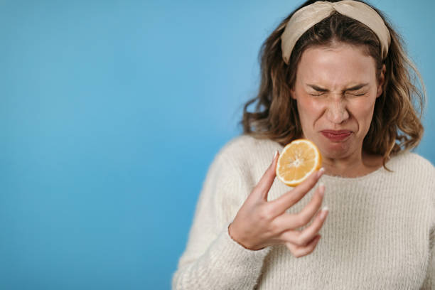 Tasty and our Woman standing in front of blue background eating lemon sour taste stock pictures, royalty-free photos & images