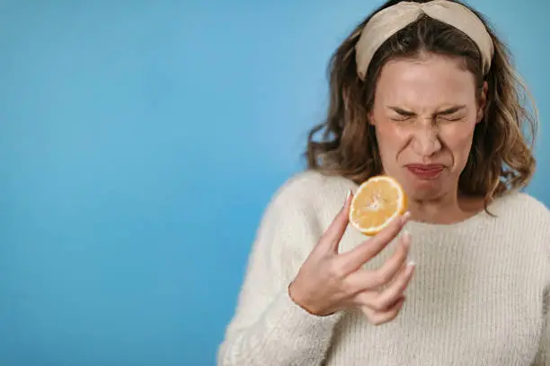 Woman standing in front of blue background eating lemon