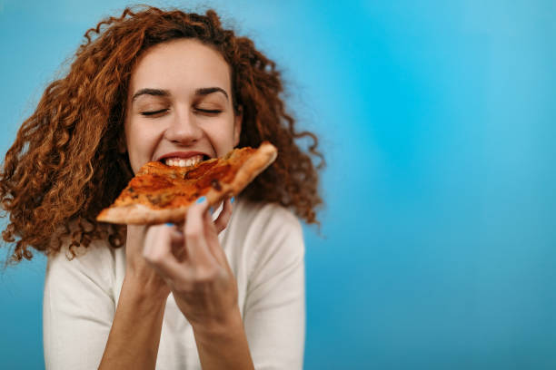 Woman standing in front of blue background and eating pizza stock photo