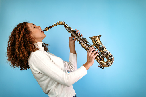 Woman standing in front of blue background and holding saxophone