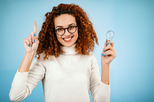 Woman standing in front of blue background holding light bulb