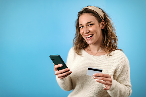 Woman standing in front of blue background paying online with credit card