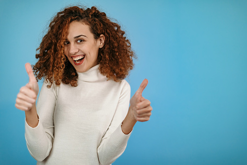 Woman standing in front of blue background with thumbs up