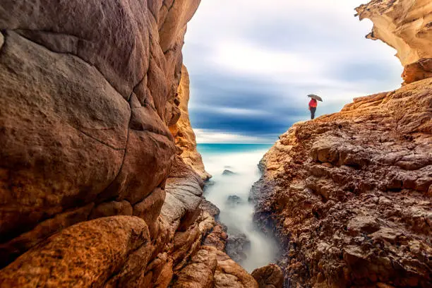 Photo of Long exposure landscape of the cave, sea and a woman with umbrella in Akyar, Silifke, Mersin, Turkey.