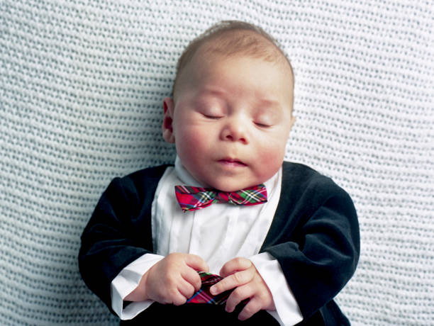 Close-up of baby Latino baby boy dressed in Tuxedo, with his eyes closed.