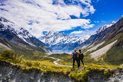 Adventurous couple standing on mountain top with view of valley and snow capped mountain range