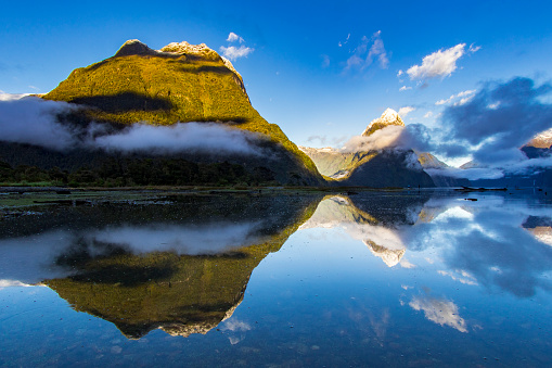Tall mountains coming up from the fiord with perfect reflection on water during sunrise, Milford Sound New Zealand