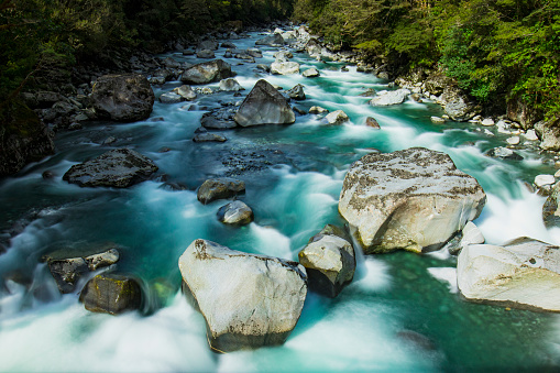 Flowing river of turquoise water and granite boulders in the new Zealand mountain ranges