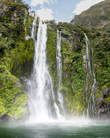 Powerful waterfall flowing into the ocean from the mountains and fiords of picturesque Milford Sound, New Zealand.