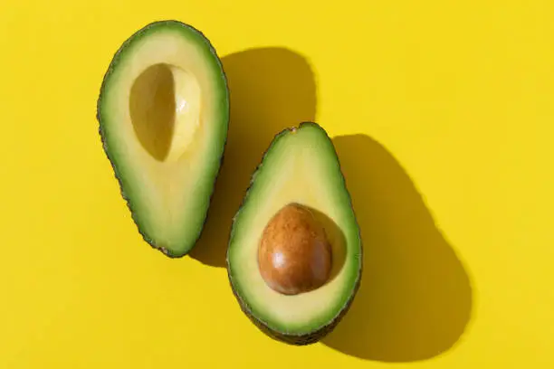 Avocado halves close up with trendy hard shadow and hard light on yellow background, minimalist