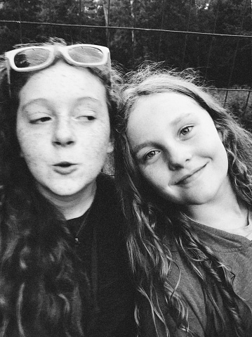 Half sisters playing and laughing and hanging out in a meadow in their yard. Series of grainy black and white vintage filtered photographs.