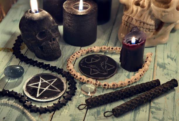 istock Pentagram and devil symbols with black burning candles on witch wooden table. 1299029070