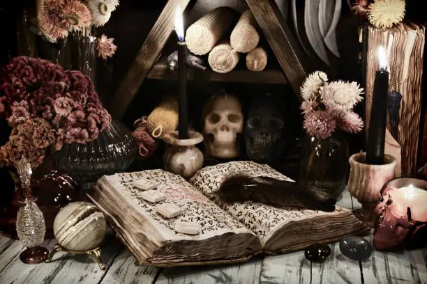 Photo of Still life with old grimoire book of magic spells, runes and evil candles on witch table.