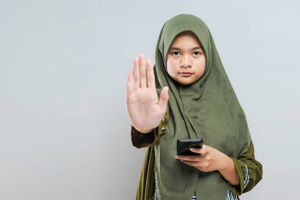 いじめのジェスチャーを止めて携帯電話を持っている若いイスラム教徒の女性 - teenager smart phone young women teenagers only ストックフォトと画像