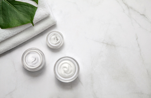 Cosmetic cream container jars with towel and leaf on marble background. Natural beauty product concept. Flat lay, top view.
