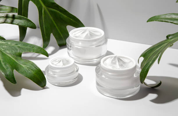 istock Cosmetic cream container jars with green leaves on white background. Blank label for branding mock-up. Natural beauty product concept. 1299041528