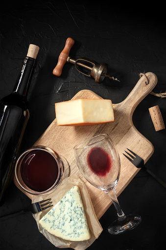 Wine and cheese tasting, shot from the top on a black background, with a vintage corkscrew and a bottle