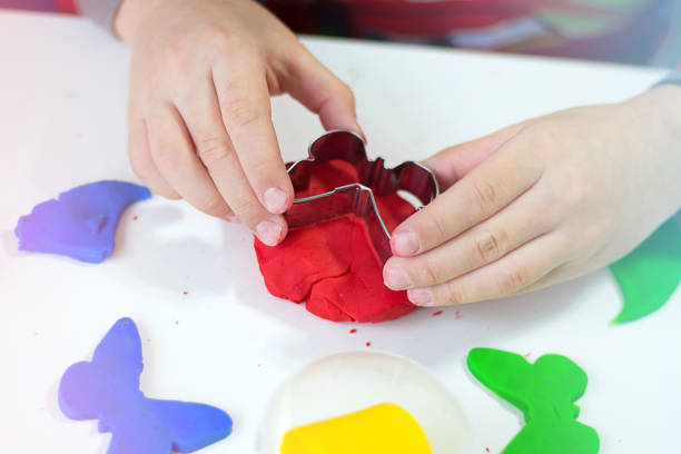 Close up of child's hands using forms for shaping and sculpting toy plasticine or dough. Child hobby on school desk at home