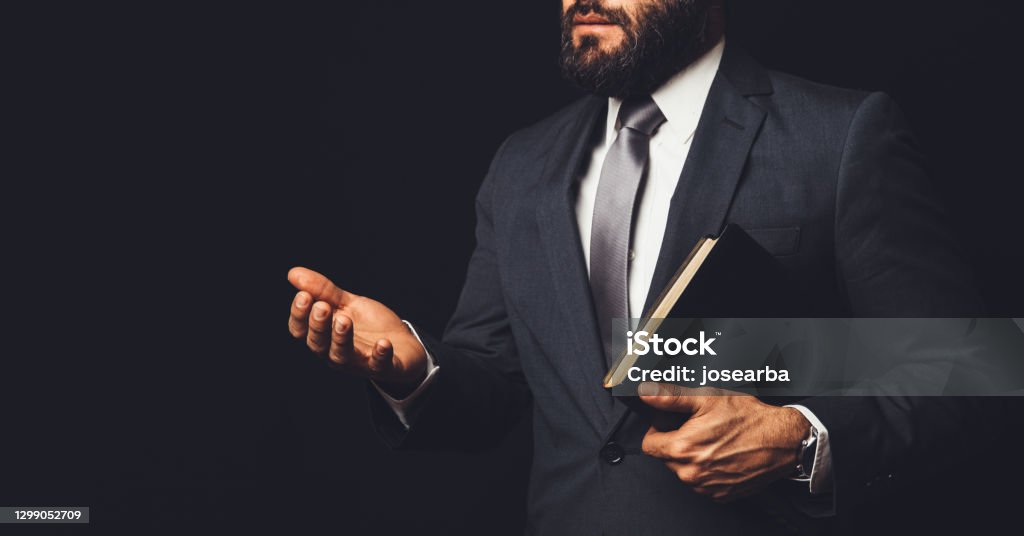 a man in a suit holding a bible in his arm speaking to another person on a black background Pastor Stock Photo
