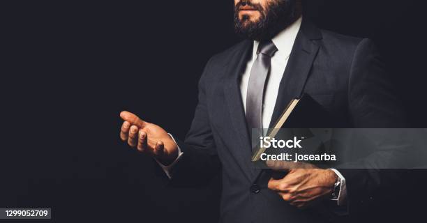 A Man In A Suit Holding A Bible In His Arm Speaking To Another Person On A Black Background Stock Photo - Download Image Now