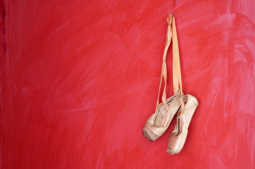 Pointe shoes hanged on red colored wall. No people are seen in frame. Shot with a full frame mirrorless camera under daylight. Panning to right camera motion effect is applied.