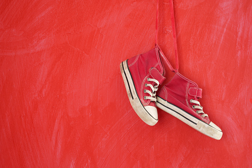 pair of red canvas shoes hanged on red colored grunge wall. No people are seen in frame. Shot with a full frame mirrorless camera.